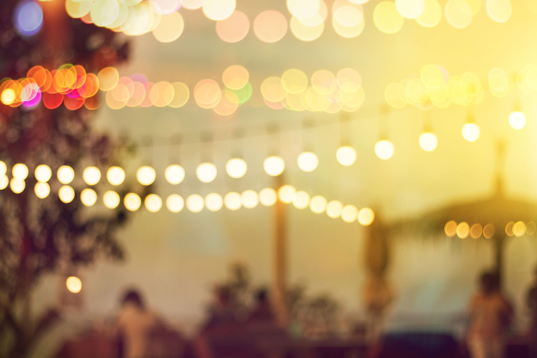 Blurred Bokeh Light On Sunset With Yellow String Lights Decor In Beach Restaurant